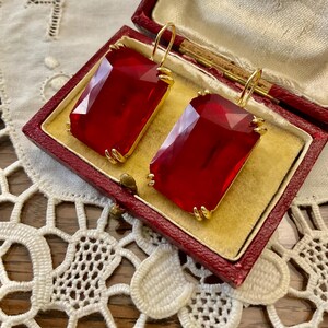 May include: A pair of red glass earrings with gold-toned metal settings. The earrings are in a small red box.