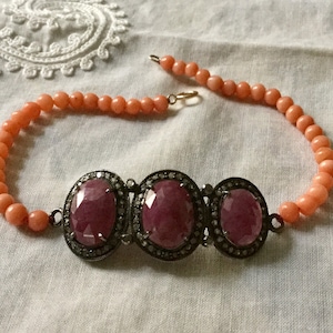 Peut inclure: Un collier de perles de corail rose avec un pendentif en argent orné de trois grandes pierres précieuses roses ovales entourées de petites pierres précieuses claires.