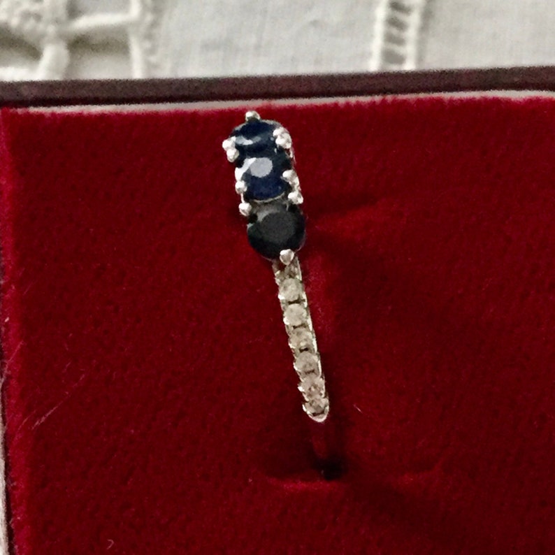 May include: A silver ring featuring three round blue sapphires and a row of small clear diamonds.