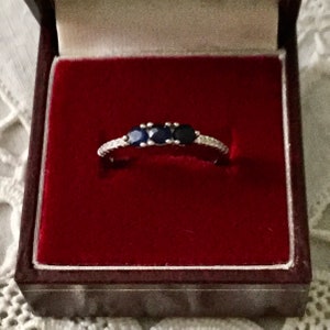 May include: A silver ring with three blue sapphires and a row of small diamonds.