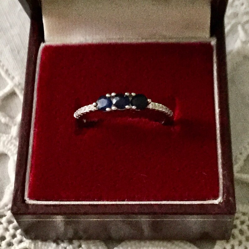 May include: A silver ring with three blue sapphires and a row of small diamonds.