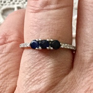May include: A silver ring with three dark blue gemstones and a row of small clear gemstones around the band.
