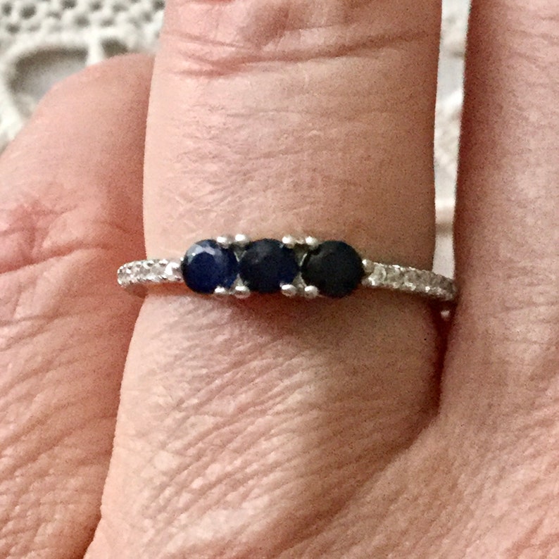May include: A silver ring with three dark blue gemstones and a row of small clear gemstones around the band.
