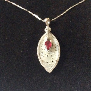 Peut inclure: Un collier en argent avec un pendentif en coquille blanche orné d'une pierre précieuse rouge en forme de cœur. Le pendentif présente un design délicat et complexe.