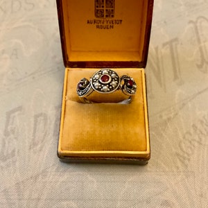 Peut inclure: Une bague en argent avec trois pierres précieuses rouges et des accents de perles. La bague est dans une boîte avec le texte "AU ROY YVETOT ROUEN".