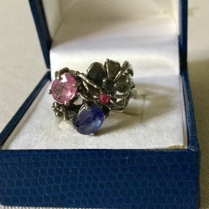 May include: A silver ring with a floral design featuring pink, blue and red gemstones.