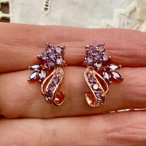 Peut inclure: Une paire de boucles d'oreilles en or avec un motif floral. Les boucles d'oreilles sont ornées de pierres précieuses violettes.