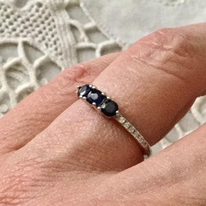 May include: A silver ring featuring three dark blue oval-shaped gemstones and a band of smaller clear gemstones.