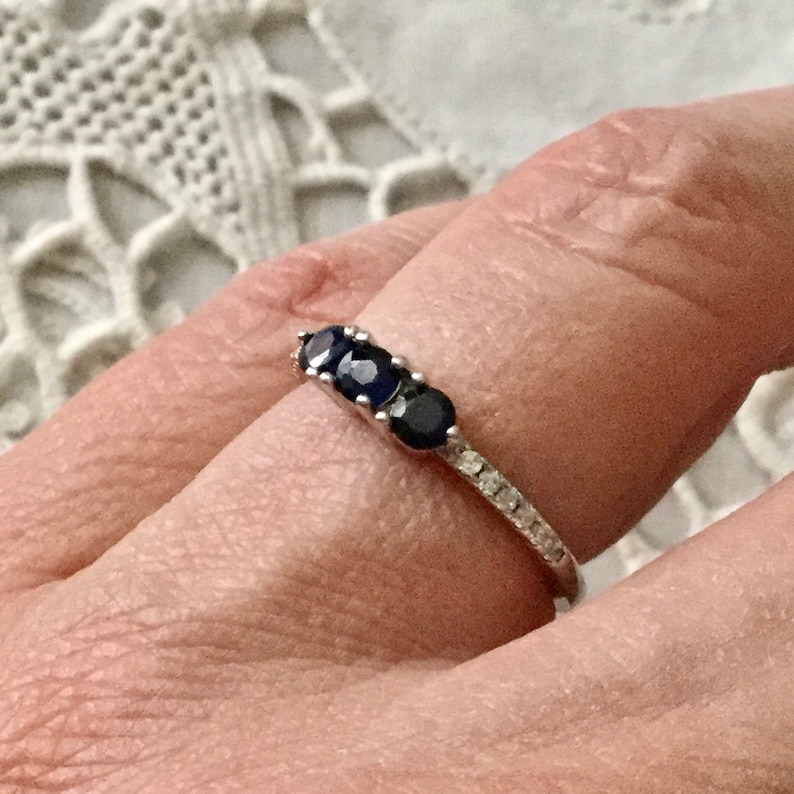 May include: A silver ring featuring three dark blue oval-shaped gemstones and a band of smaller clear gemstones.