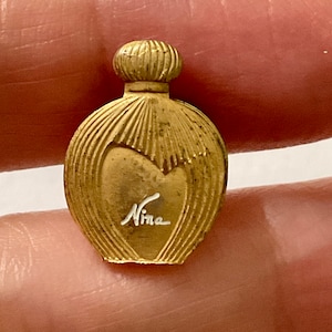 Peut inclure: Flacon de parfum de couleur or avec un motif en forme de cœur et le mot "Nina" inscrit sur le devant.
