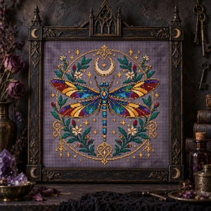 May include: A cross-stitch embroidery featuring a vibrant dragonfly with blue, yellow, and purple wings, centred within a circular floral wreath and a crescent moon. The artwork is displayed in a dark, ornate, gothic-style rectangular frame.