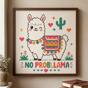 May include: A framed cross-stitch embroidery featuring a white winking llama with a colorful patterned saddle, surrounded by small hearts, flowers, and a cactus. The text NO PROBLLAMA is stitched in multicolored letters at the bottom of the piece.