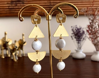 May include: Gold geometric earrings with white pearl accents. The earrings feature a triangle, a half-circle, and a pearl bead.