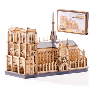 May include: A wooden model of the Paris Cathedral, featuring intricate architectural details. The model is light brown with gray accents and sits on a gray base. A box with the words "Paris Cathedral" is visible in the background.
