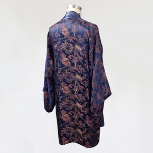 May include: A navy blue silk robe with a floral pattern in shades of pink and gold. The robe has long sleeves and a wide collar.