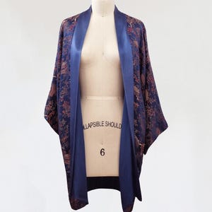 May include: A navy blue and brown patterned kimono with a satin trim. The kimono is open in the front and has a long, flowing silhouette.