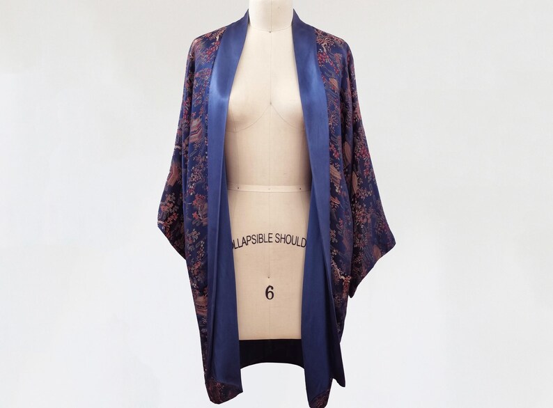 May include: A navy blue and brown patterned kimono with a satin trim. The kimono is open in the front and has a long, flowing silhouette.