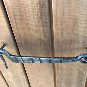 May include: A black metal door handle with a decorative design. The handle is attached to a wooden door with screws.