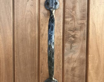 May include: A black metal door handle with a hammered finish and a pointed design. The handle is attached to a wooden door.