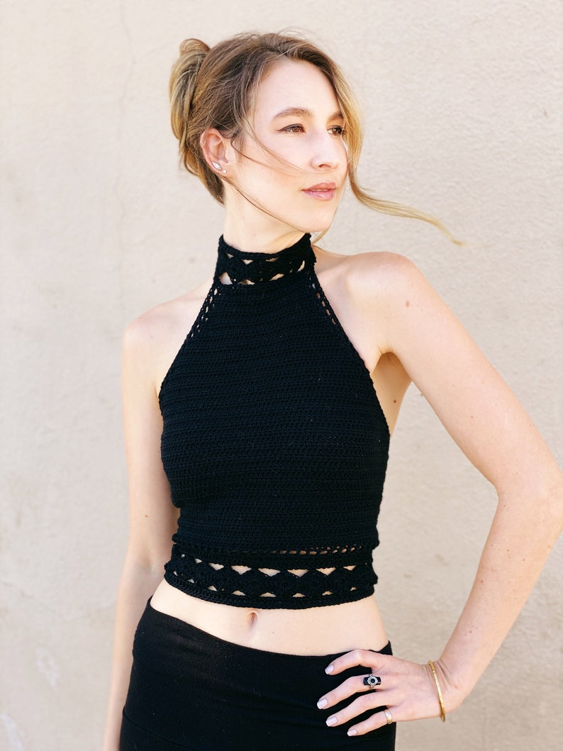May include: A black crochet halter top with a high neckline and a crocheted trim around the bottom. The top is cropped and shows the model's midriff.