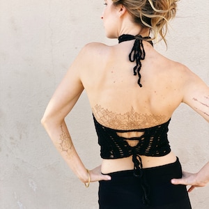 May include: A black crochet halter top with a lace-up back and a geometric design on the back. The top is worn with a black skirt.