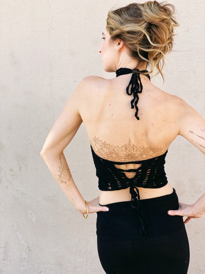 May include: A black crochet halter top with a lace-up back and a geometric design on the back. The top is worn with a black skirt.