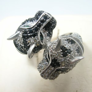 Könnte beinhalten: Ein silberner Ring mit zwei schwarzen und weißen Pantherköpfen, jeder Kopf ist mit schwarzen und weißen Diamanten besetzt.