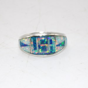 May include: A silver ring with a blue, white, and green opal inlay. The opal is set in a square shape and is surrounded by a silver band.