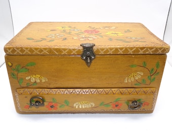 May include: A wooden box with a floral design painted on the lid and front. The box has a hinged lid with a metal latch and a small drawer on the front.