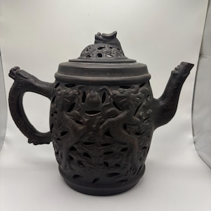 Op de afbeelding: Donkerbruine keramische theepot met ingewikkelde draken- en bloemuitsparingen. De theepot heeft een draakvormige handgreep en tuit, en een deksel met een drakenfiguur. Een uniek decoratief stuk.