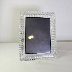 May include: A rectangular picture frame made of clear, faceted glass. The frame features a prominent diamond-cut pattern along the border, creating a textured, reflective surface around a dark, solid-colored rectangular center insert.