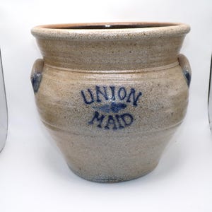 Puede incluir: Un tarro de barro con un logotipo "Union Maid" azul y blanco. El tarro tiene dos asas y una superficie texturizada.