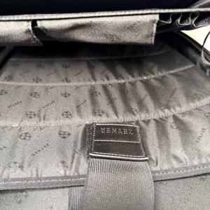 May include: Black interior of a bag with a fabric lining. The lining has a repeating pattern. A black strap with the word "ZEYNER" is sewn into the bag.