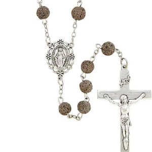 Könnte beinhalten: Eine silberne Rosenkranz mit braunen Lavasteinperlen, einem silbernen Kruzifix mit der Inschrift "INRI" und einem silbernen ovalen Anhänger mit einer Darstellung der Jungfrau Maria.