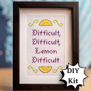 May include: A framed cross-stitch pattern with the text "Difficult, Difficult, Lemon, Difficult" and a lemon image above and below the text. The frame is brown wood and the text is purple. A speech bubble with the text "DIY Kit" is in the lower right corner of the image.