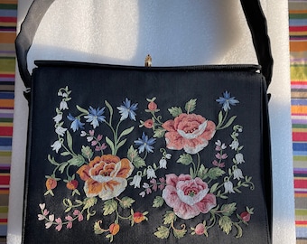May include: A black handbag with a floral embroidered design. The embroidery features pink, red, and yellow roses with green leaves and white flowers.