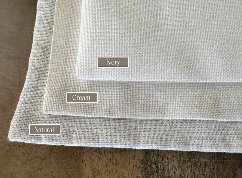 May include: Three fabric swatches in different shades of white: natural, cream, and ivory. The swatches are stacked on top of each other, with the natural swatch at the bottom and the ivory swatch at the top.