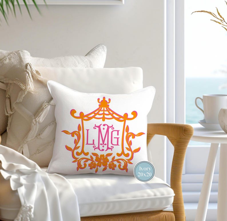May include: A white pillow with a monogram design featuring the letters LMG in pink. The monogram is surrounded by an orange floral design. The pillow is 20x20 inches and is labeled "Ivory".