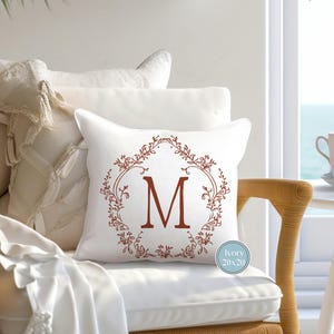 May include: White throw pillow with a red monogram "M" in a decorative floral wreath. The pillow is 20 inches by 20 inches and has the text "Ivory 20x20" printed on the bottom right corner.