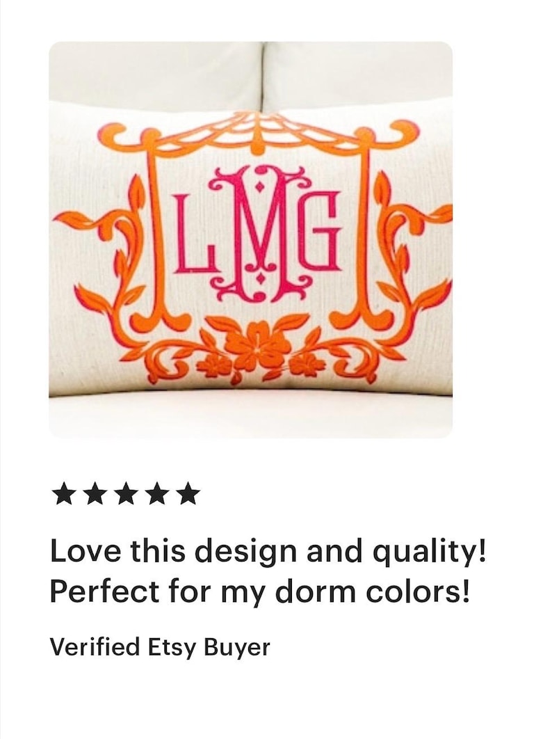 May include: A white pillow with an orange and pink monogram of the letters "LMG" in a decorative frame. The pillow is embroidered with floral details.