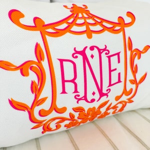 May include: A white pillow with an orange and pink monogram design. The monogram is "RNE" and is surrounded by a decorative frame with a floral design.