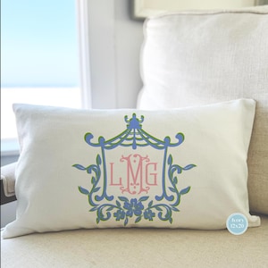 May include: A white pillow with a green, blue, and pink monogram design. The monogram is in a decorative frame with floral accents. The pillow is 12x20 inches and is labeled "ivory".