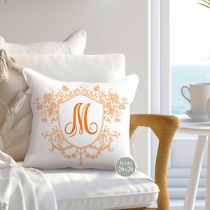 May include: A white throw pillow with an orange embroidered monogram "M" in a decorative frame. The pillow is 20 inches by 20 inches.