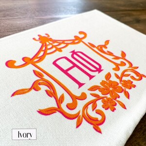 May include: A white canvas tote bag with an orange and pink monogram design. The monogram is a stylized "HO" with a floral design around it. The bag is labeled "ivory".