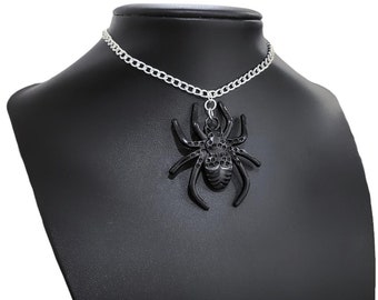 May include: A black spider pendant necklace with a silver chain. The spider pendant has a detailed design and is displayed on a black mannequin. The necklace is a gothic or Halloween-themed accessory.