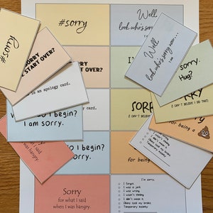 Peut inclure: Un jeu de cartes color&eacute;es avec diff&eacute;rentes phrases li&eacute;es aux excuses, notamment "#sorry", "D&eacute;sol&eacute;, recommencer ?", "Je suis d&eacute;sol&eacute;", "Eh bien, voil&agrave; qui s'excuse maintenant...", "D&eacute;sol&eacute;, c&acirc;lin ?", et "Je n'arrive pas &agrave; croire que j'ai fait &ccedil;a".