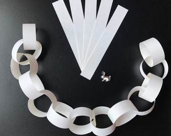 May include: White paper chain links made from strips of paper. The chain is laid out in a circle on a black surface. There are five white strips of paper next to the chain.