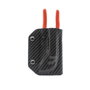 Puede incluir: Una funda de fibra de carbono negra con dos bucles rojos para llevar una herramienta. La funda tiene dos tornillos negros en el lateral.