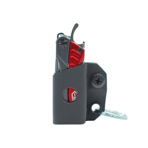 Könnte beinhalten: Ein graues Multitool mit rotem Griff ist an einem grauen Lederetui mit einem Schlüsselring befestigt. Das Etui hat eine Schraube an der Seite und einen Ausschnitt für das Markenlogo.