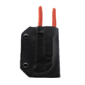 Puede incluir: Una funda de cuero negra con dos asas rojas. La funda tiene dos tornillos en el lateral.